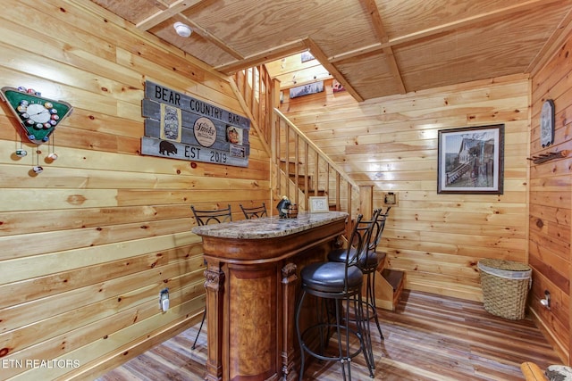 bar with stairs, wooden walls, wood finished floors, and a bar