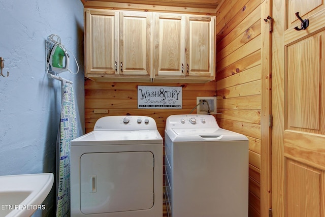 clothes washing area featuring cabinet space, independent washer and dryer, wood walls, and a textured wall