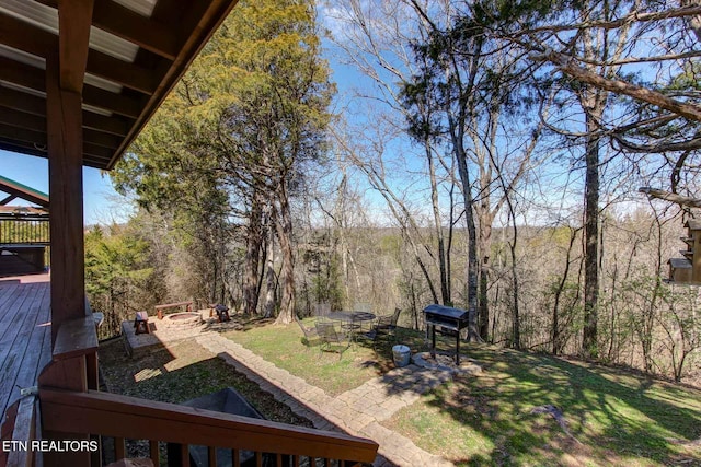 view of yard featuring a wooden deck, a wooded view, and an outdoor fire pit