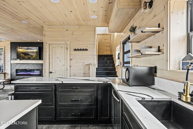 kitchen with open floor plan, wooden ceiling, black microwave, wood walls, and dark cabinets