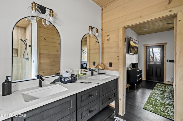 full bath with double vanity, wooden walls, wood finished floors, and a sink