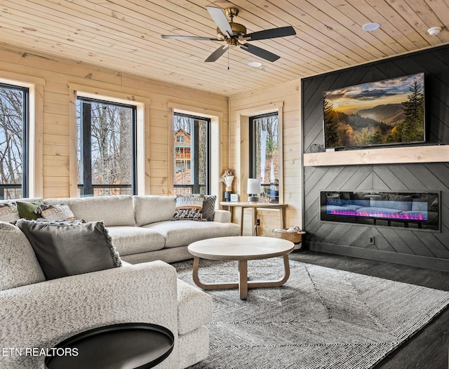 living room featuring a glass covered fireplace, wooden ceiling, wooden walls, and a wealth of natural light