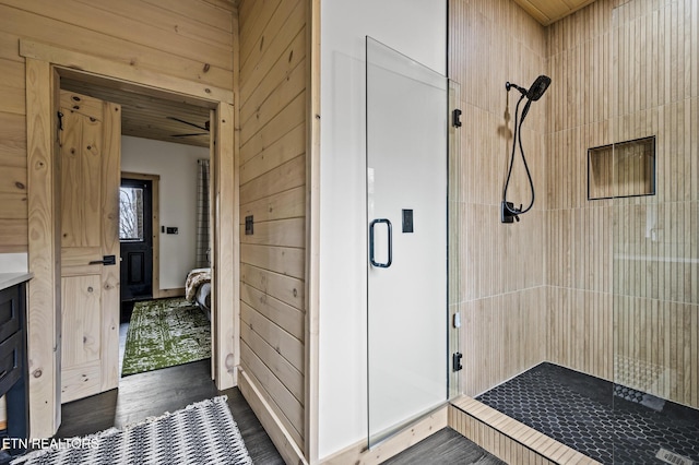 bathroom featuring wooden walls, a shower stall, and wood finished floors