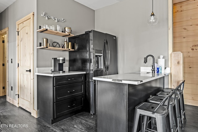 kitchen featuring dark cabinetry, a breakfast bar area, dark wood finished floors, light countertops, and black fridge