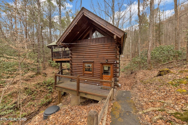 view of property exterior with log siding, a deck, a wooded view, and a balcony