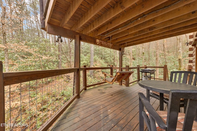 wooden terrace featuring outdoor dining area and a wooded view