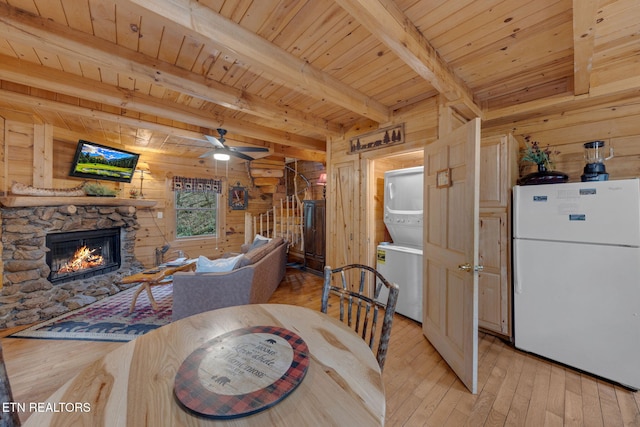 dining room with wooden walls, light wood-type flooring, stairs, a fireplace, and stacked washing maching and dryer