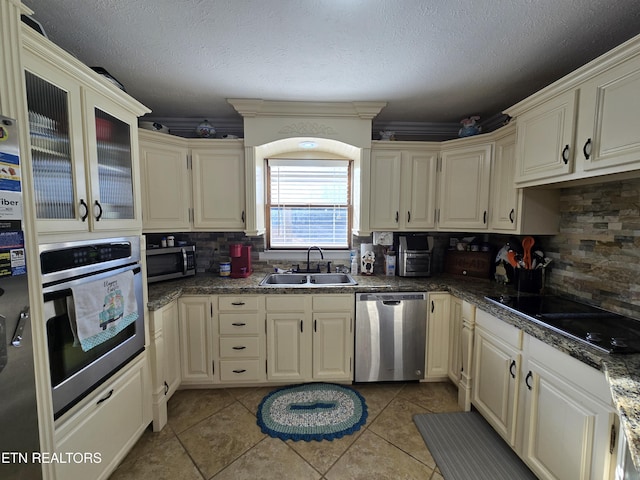 kitchen featuring dark countertops, backsplash, appliances with stainless steel finishes, a textured ceiling, and a sink