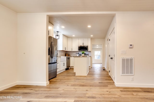 kitchen featuring light wood-type flooring, visible vents, backsplash, white cabinetry, and stainless steel appliances