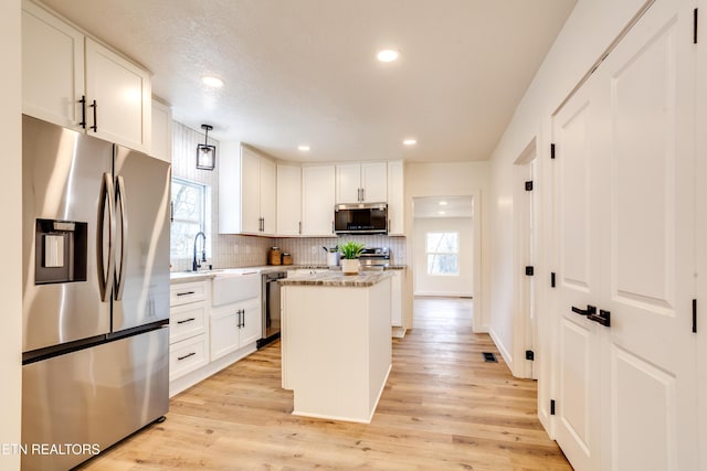 kitchen featuring appliances with stainless steel finishes, a kitchen island, light wood-style floors, and a sink