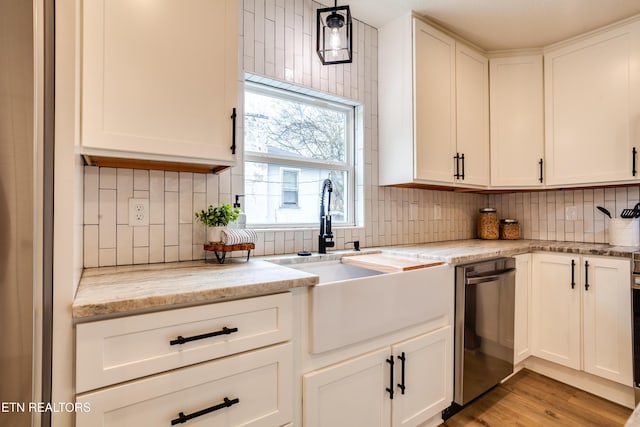 kitchen with stainless steel dishwasher, white cabinets, backsplash, and a sink