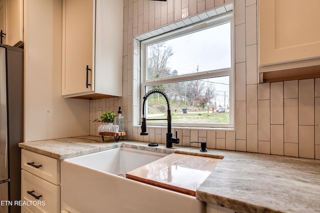 kitchen with white cabinetry, backsplash, freestanding refrigerator, and a sink