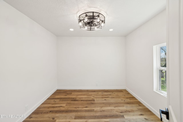 empty room featuring a textured ceiling, light wood finished floors, baseboards, recessed lighting, and a notable chandelier