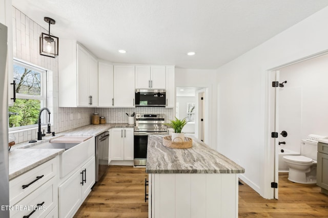 kitchen featuring a sink, a kitchen island, tasteful backsplash, stainless steel appliances, and light wood-style floors