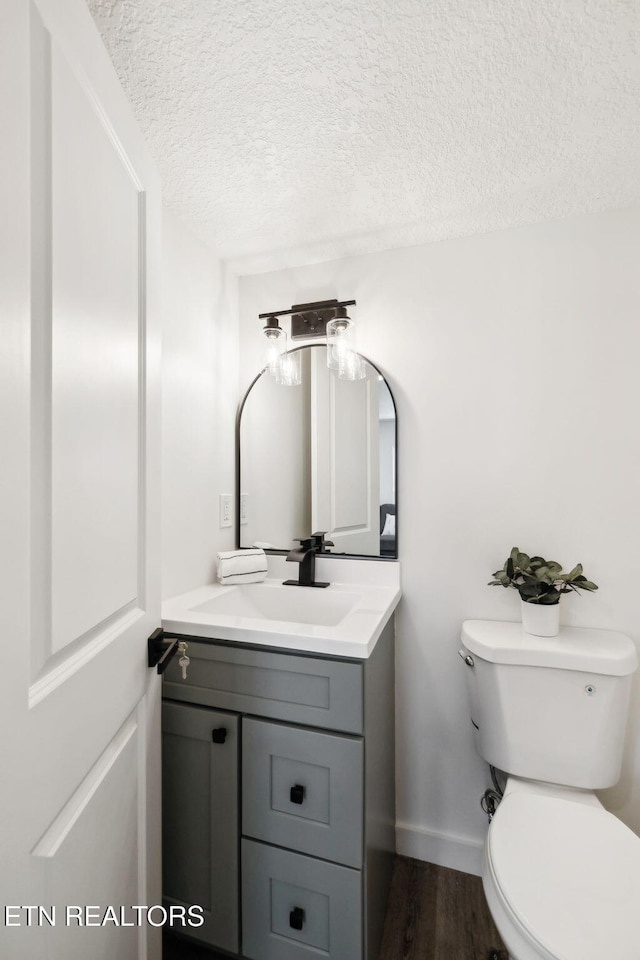 bathroom with vanity, toilet, baseboards, a textured ceiling, and wood finished floors