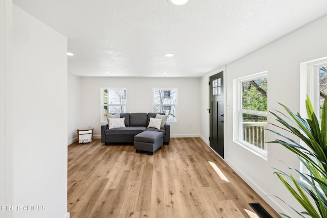 sitting room featuring baseboards, a textured ceiling, visible vents, and light wood finished floors