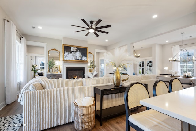 living room featuring recessed lighting, a glass covered fireplace, wood finished floors, and ceiling fan with notable chandelier