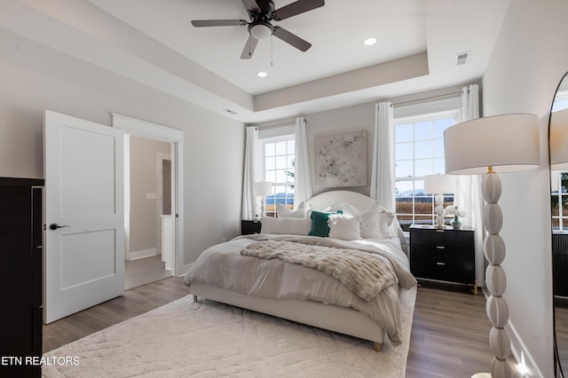 bedroom featuring recessed lighting, baseboards, a tray ceiling, and wood finished floors