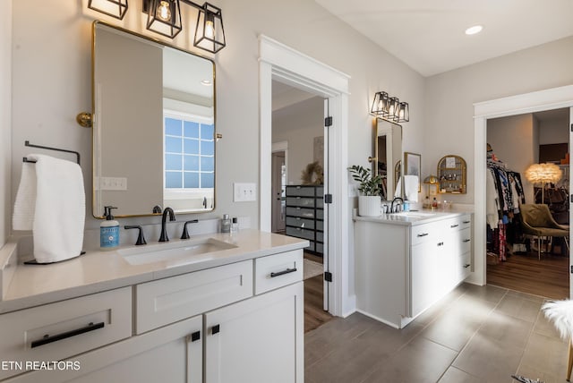 full bathroom featuring a walk in closet, two vanities, wood finished floors, and a sink