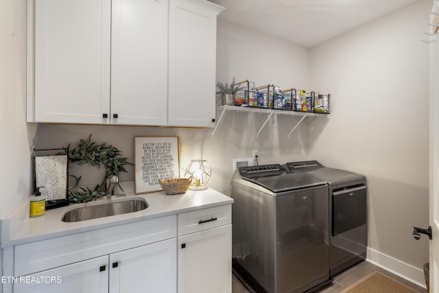 laundry room with a sink, baseboards, cabinet space, and independent washer and dryer