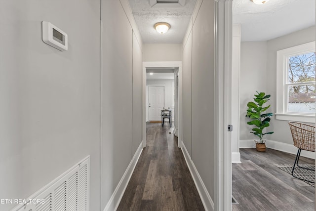 corridor with dark wood finished floors, visible vents, a textured ceiling, and baseboards