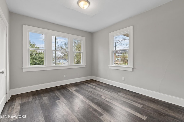 spare room featuring dark wood-type flooring, visible vents, and baseboards