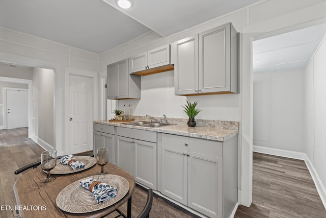 kitchen featuring gray cabinetry, baseboards, dark wood-style flooring, and a sink