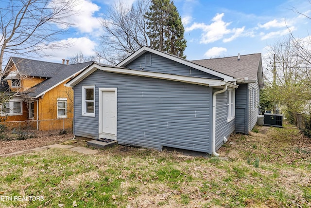 rear view of property featuring cooling unit, roof with shingles, and fence