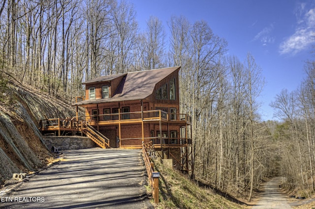 view of side of property with stairs, a gambrel roof, a wooded view, and driveway