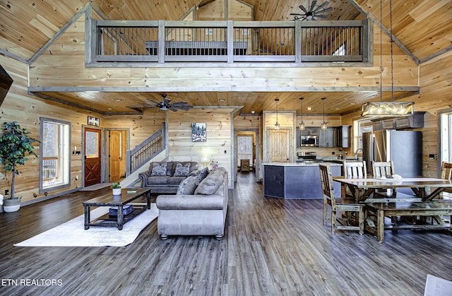 living area featuring stairs, wooden walls, dark wood-style flooring, and a ceiling fan