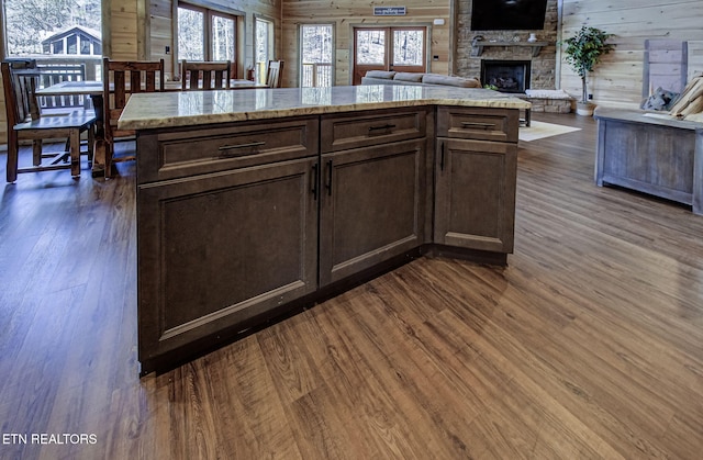 kitchen with dark wood-type flooring, dark brown cabinets, a fireplace, and wood walls