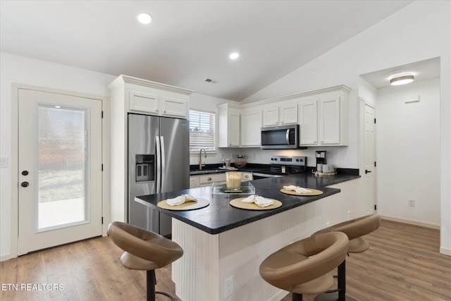 kitchen featuring a breakfast bar, a sink, stainless steel appliances, white cabinets, and dark countertops