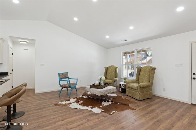 living area with visible vents, wood finished floors, baseboards, and vaulted ceiling