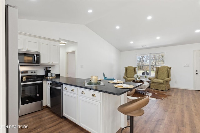 kitchen with a peninsula, dark wood-style flooring, vaulted ceiling, appliances with stainless steel finishes, and white cabinetry