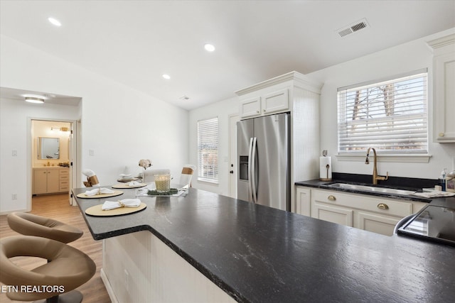 kitchen featuring visible vents, lofted ceiling, stainless steel fridge with ice dispenser, a sink, and dark countertops