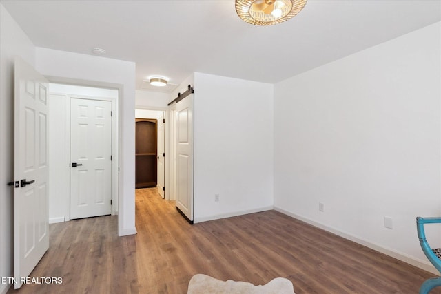 unfurnished bedroom featuring a barn door, wood finished floors, and baseboards