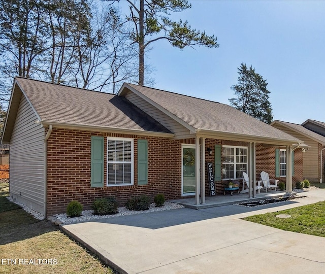 ranch-style home with brick siding, a patio, and roof with shingles