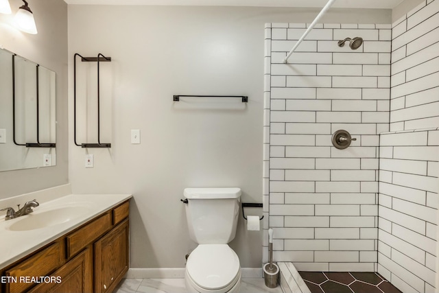 bathroom with vanity, toilet, baseboards, and tiled shower