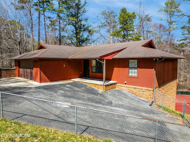 view of front of home with roof with shingles, driveway, and fence