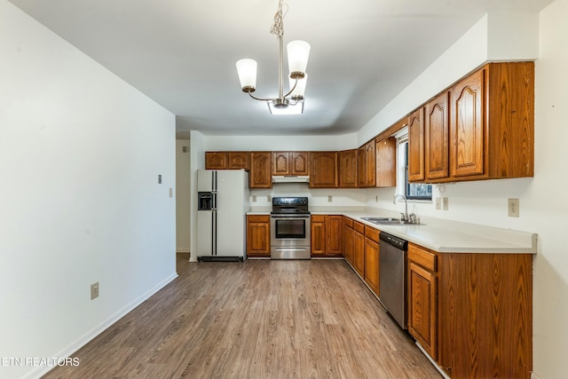 kitchen featuring wood finished floors, brown cabinetry, a sink, stainless steel appliances, and under cabinet range hood