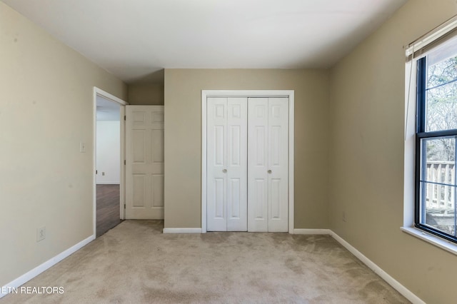 unfurnished bedroom featuring a closet, light colored carpet, and baseboards