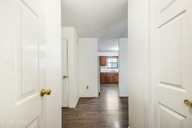 hallway with dark wood-type flooring, baseboards, and a sink