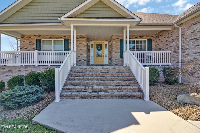 doorway to property featuring brick siding and a porch