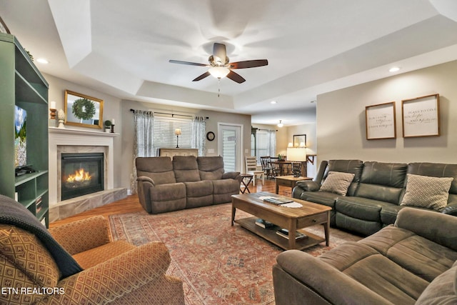 living area with wood finished floors, a ceiling fan, a fireplace, recessed lighting, and a raised ceiling