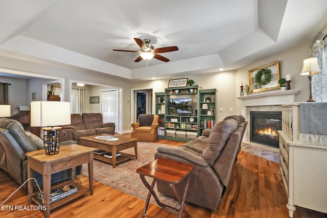 living area featuring light wood-style floors, a raised ceiling, and ceiling fan