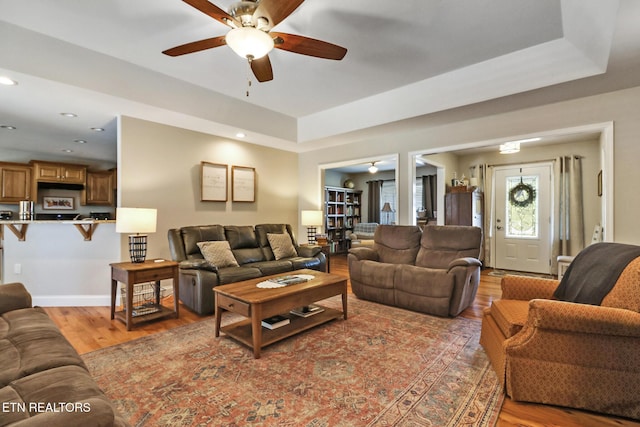 living area with light wood finished floors, baseboards, a tray ceiling, and ceiling fan