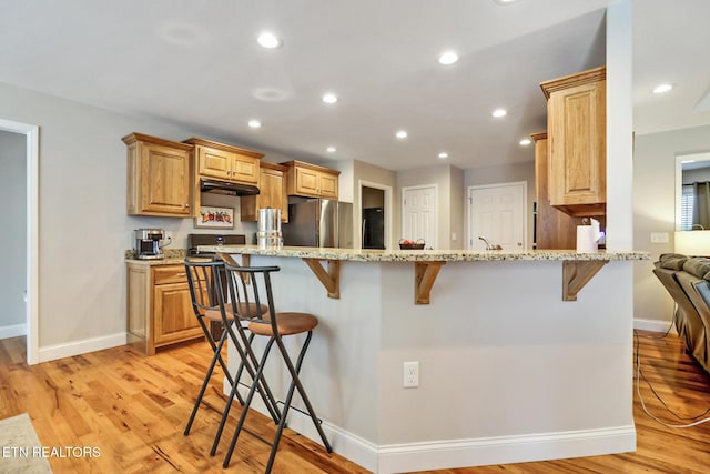 kitchen with light wood finished floors, recessed lighting, a breakfast bar area, and freestanding refrigerator