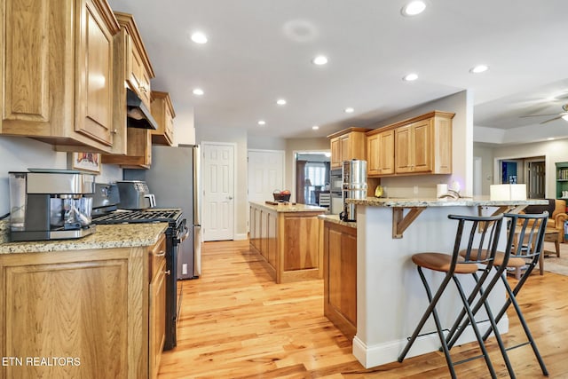 kitchen featuring light wood-style flooring, a kitchen bar, stainless steel range with gas stovetop, and a center island