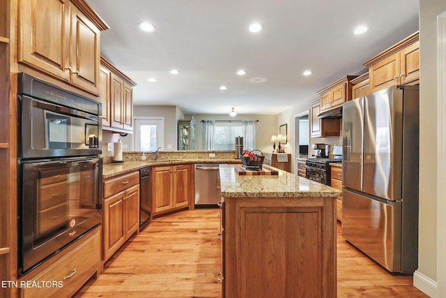 kitchen with black appliances, light stone counters, a center island, light wood-style floors, and a peninsula