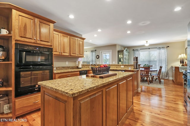 kitchen with dobule oven black, light stone counters, a center island, light wood-style floors, and a peninsula